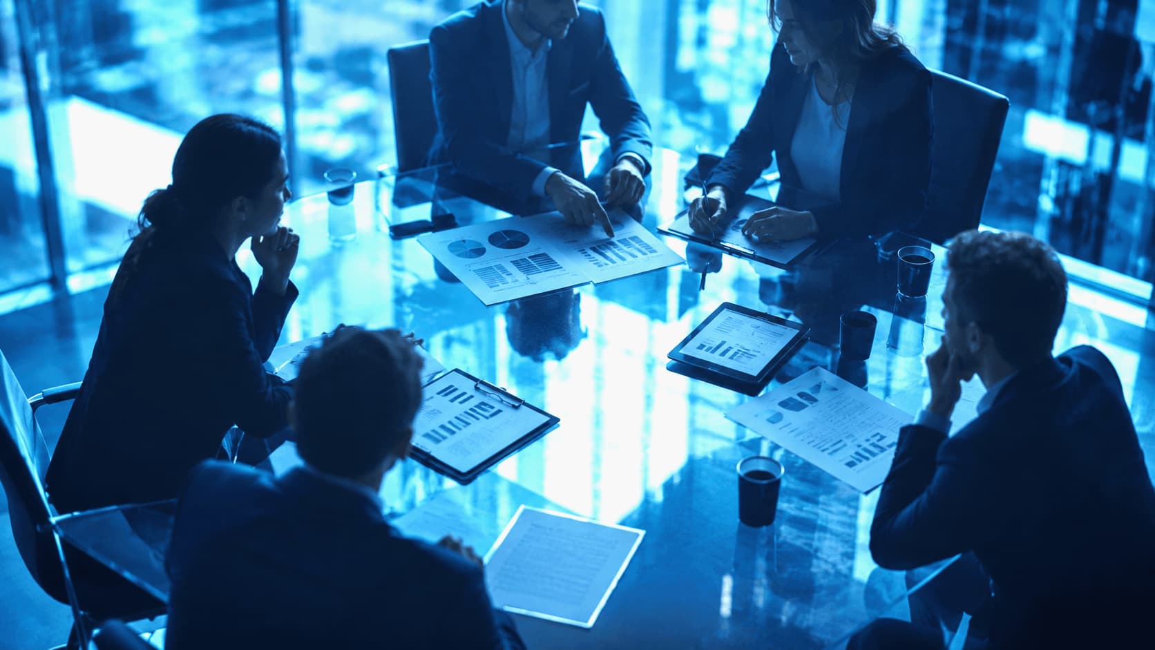 Equipo de trabajo reunido en una mesa ejecutiva con gráficos y reportes en tonos azules